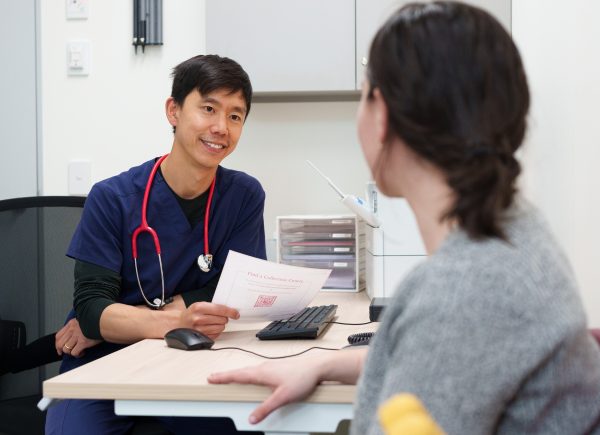 Smiling doctor wearing scrubs with a patient who is wearing a grey top.