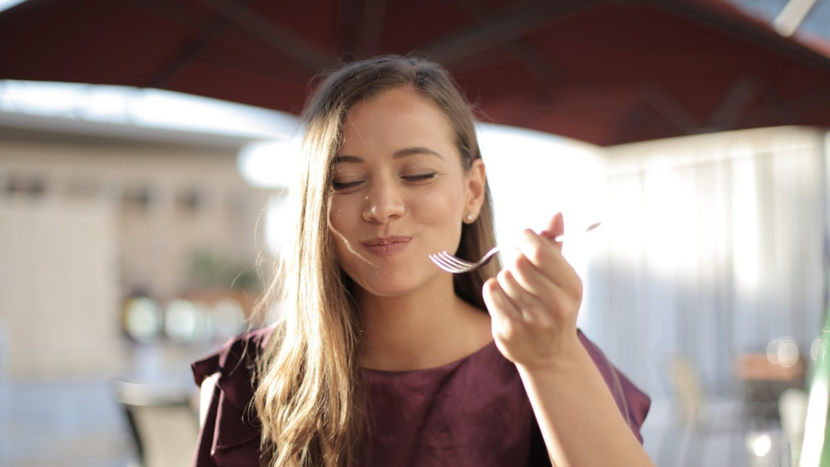 Woman smiles with mouth full, hand holding fork near her face